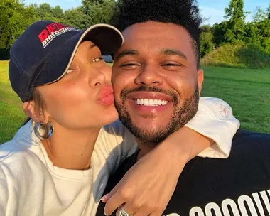 Two people posing for a cheerful selfie outdoors, one kissing the other's cheek.