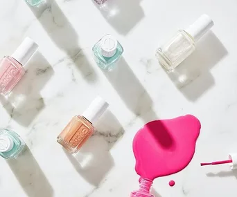 Various nail polish bottles on a marble surface with pink polish spilled, highlighting summer pedicure colors.