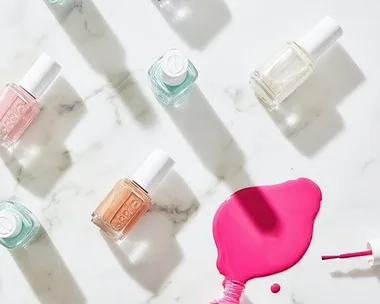 Various nail polish bottles on a marble surface with pink polish spilled, highlighting summer pedicure colors.