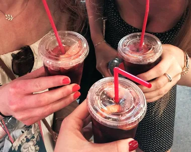 Close-up of three people holding plastic cups of iced drinks with red straws.