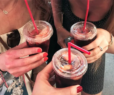 Close-up of three people holding plastic cups of iced drinks with red straws.