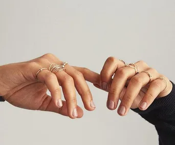 Close-up of hands with minimalist rings on each finger, showcasing a neutral nail polish.