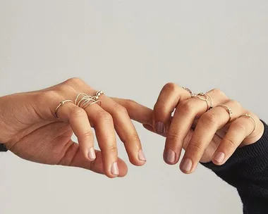 Close-up of hands with minimalist rings on each finger, showcasing a neutral nail polish.