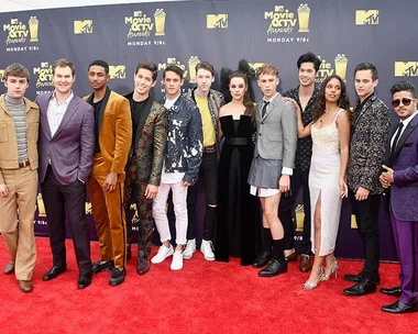 Cast of "13 Reasons Why" on the red carpet at the MTV Movie & TV Awards, posing together and smiling for the cameras.