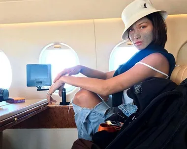 
A woman with a face mask sitting in an airplane, wearing a white hat and casual clothes.