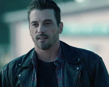 Man wearing a leather jacket and plaid shirt, standing outdoors, from Riverdale as FP Jones.