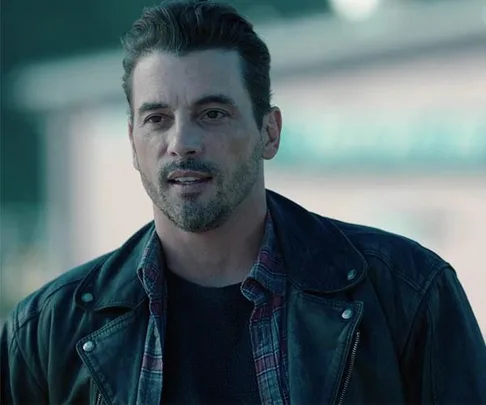 Man wearing a leather jacket and plaid shirt, standing outdoors, from Riverdale as FP Jones.