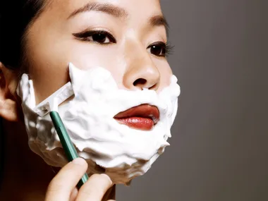 A woman with shaving foam on her face using a razor for dermablading.