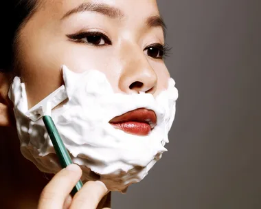 A woman with shaving foam on her face using a razor for dermablading.