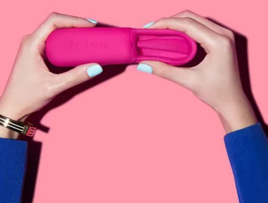 Two hands holding a pink menstrual cup in a case against a pink background.