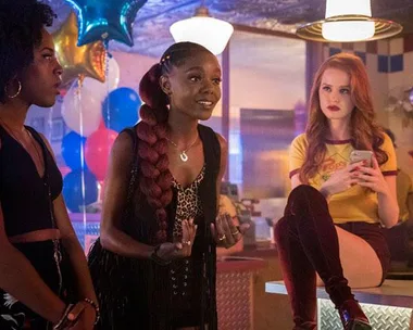 Three women in a diner, one seated on the counter, colorful balloons in the background.