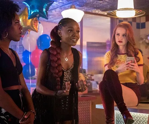 Three women in a diner, one seated on the counter, colorful balloons in the background.