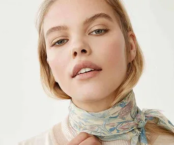 Woman wearing a light blue floral scarf around her neck, against a plain white background.