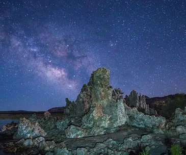 Starry night sky over rocky landscape with the Milky Way visible, highlighting rugged terrain and cosmic backdrop.