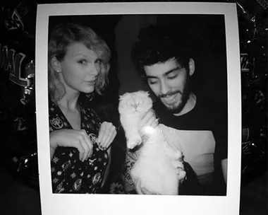 Black and white photo of two people smiling, one holding a white cat.