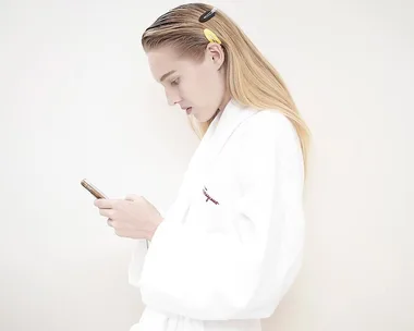 Person in a white robe looks at their phone with hair clips on the side.