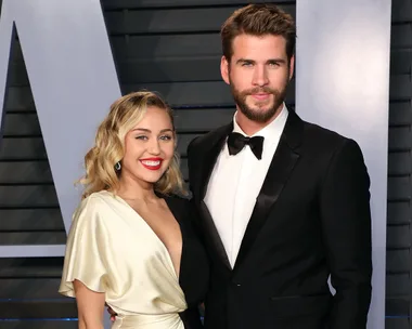 A couple in formal attire poses together at a red carpet event.