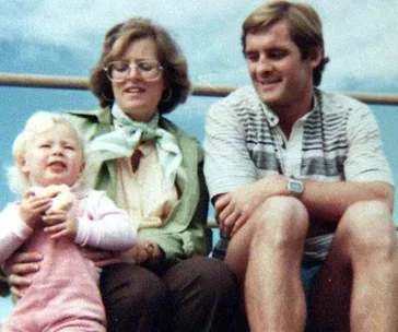 A family photo with a man, a woman, and a child sitting together outdoors.