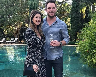 A couple stands poolside, smiling, holding champagne glasses, surrounded by lush greenery and loungers in the background.