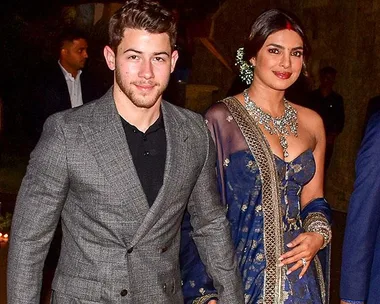 Nick Jonas and Priyanka Chopra at their second wedding reception, with Nick in a grey suit and Priyanka in a blue saree.