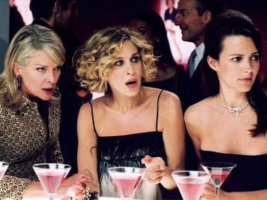 Three women from "Sex and the City" look shocked while sitting at a bar with martinis.