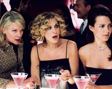 Three women from "Sex and the City" look shocked while sitting at a bar with martinis.