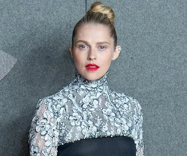 Teresa Palmer at Chanel show in Paris, wearing a floral lace top with a black section over the chest, hair in a top bun.