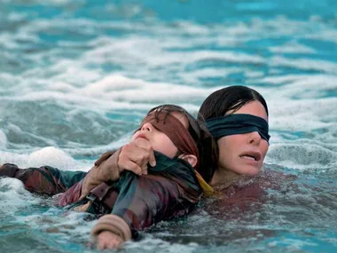 Two blindfolded characters from "Bird Box" struggle to navigate through water.