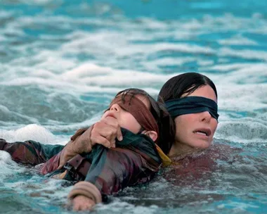 Two blindfolded characters from "Bird Box" struggle to navigate through water.