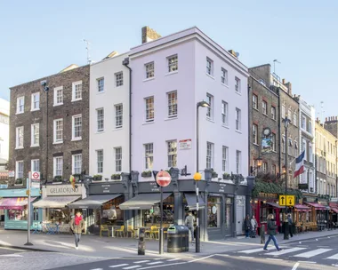 A street scene in London with cafes, shops, and pedestrians, showcasing buildings with varied architectural styles.