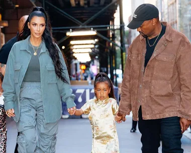 Kim Kardashian and Kanye West walking with their daughter, North West, on a city street.