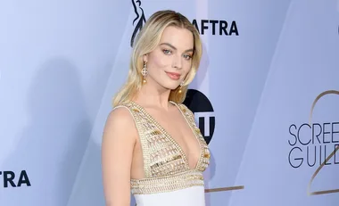 Woman in a white and gold gown at the SAG Awards 2019, posing in front of a branded backdrop.