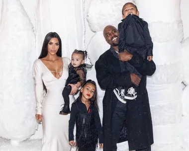 Family poses together in front of snow-like decorations, with adults dressed in formal attire and children in black outfits.