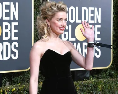 Person in elegant black dress waves at Golden Globe Awards, wearing a Time's Up ribbon on wrist.