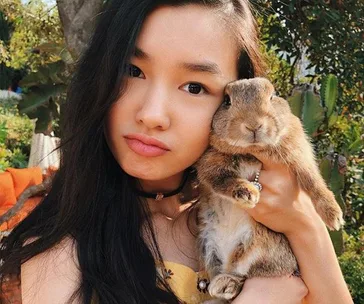 A woman holding a rabbit, both looking at the camera, in an outdoor setting.