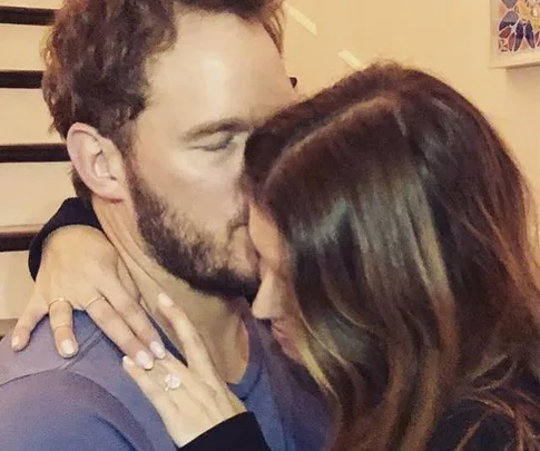 A couple embracing closely, the woman shows off her engagement ring.