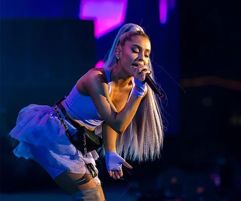 Singer performs energetically on stage with a microphone, colorful lights in the background.