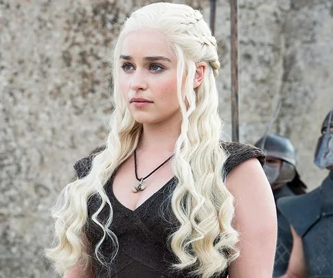 Daenerys Targaryen with long blonde hair, wearing a dark dress, standing outside in "Game of Thrones."