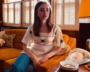 Woman in 70s-style embroidered top sits on a vintage sofa next to a rotary phone.