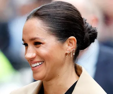 A smiling woman with a styled bun and unique earrings, set against a blurred crowd background.