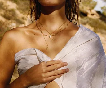 Woman wearing layered gold necklaces and a white wrap outdoors.