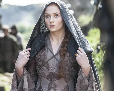 Sansa Stark wearing a hooded cloak in a scene from Game of Thrones, Season 8, outdoors with blurred background.