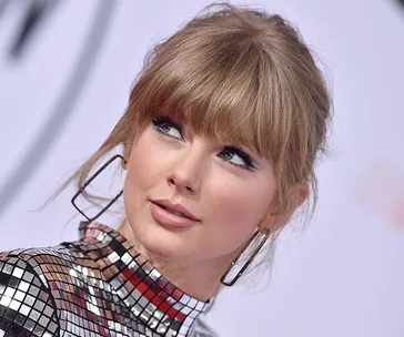 Taylor Swift at the 2019 Golden Globes, wearing a reflective sequin dress and large hoop earrings.