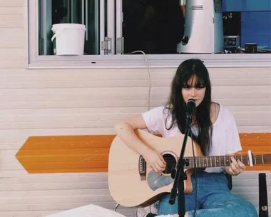 Young woman playing acoustic guitar and singing into a mic outdoors.