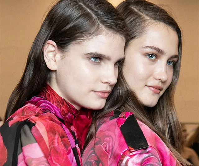 Two models with sleek hair and floral outfits at a fashion show.