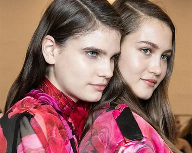 Two models with sleek hair and floral outfits at a fashion show.