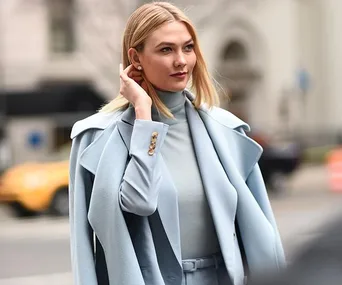 A woman in a stylish light blue outfit stands confidently on a city street.