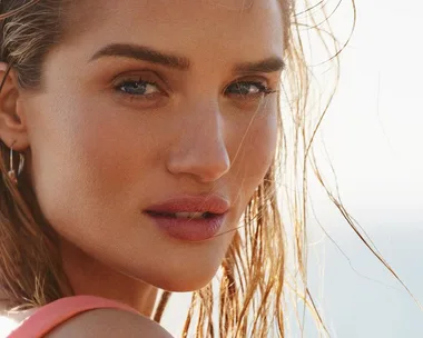 Close-up of a woman's face with wet hair, outdoors in natural light, looking towards the camera.