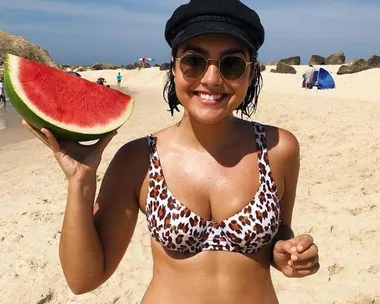 Woman in leopard bikini and sunglasses holding watermelon slice on sunny beach.