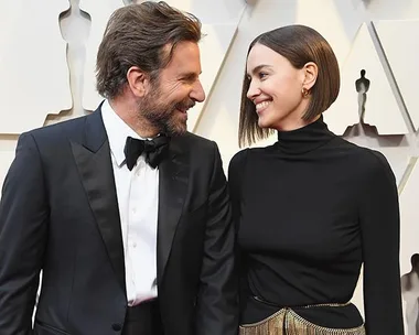 A couple dressed in formal attire smiling at each other on the red carpet at the 2019 Oscars.